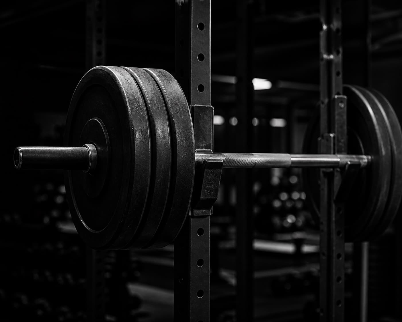 Loaded barbell on a rack, plates in focus, in high-contrast black and white